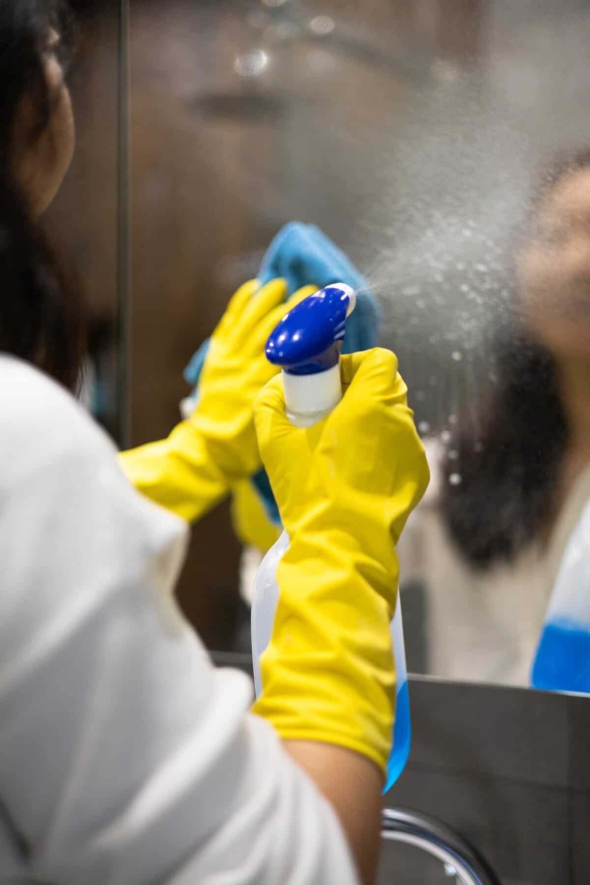 Cleaner spraying and wiping a mirror